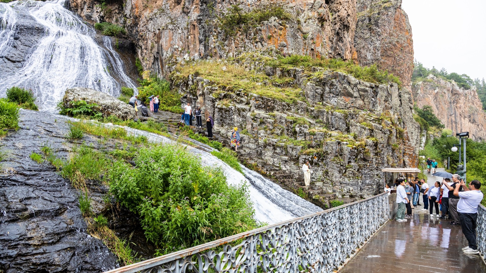 Люди возле водопада Джермук в дождливый летний день.