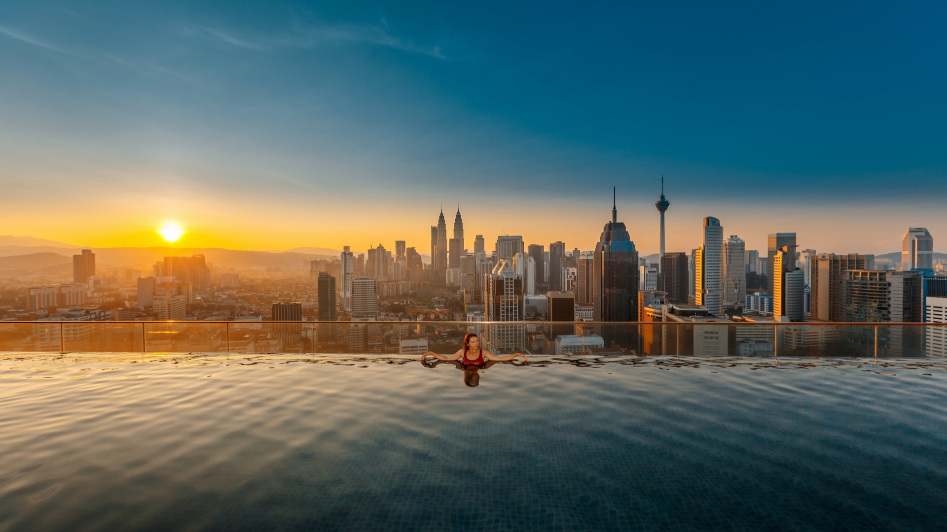 Женщина в бассейне на крыше с прекрасным видом на город Куала-Лумпур.